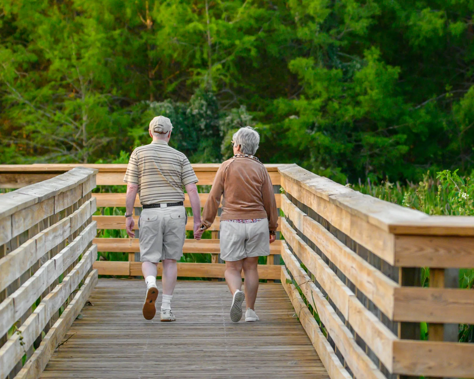 Older couple walking hand in hand along a wooden boardwalk