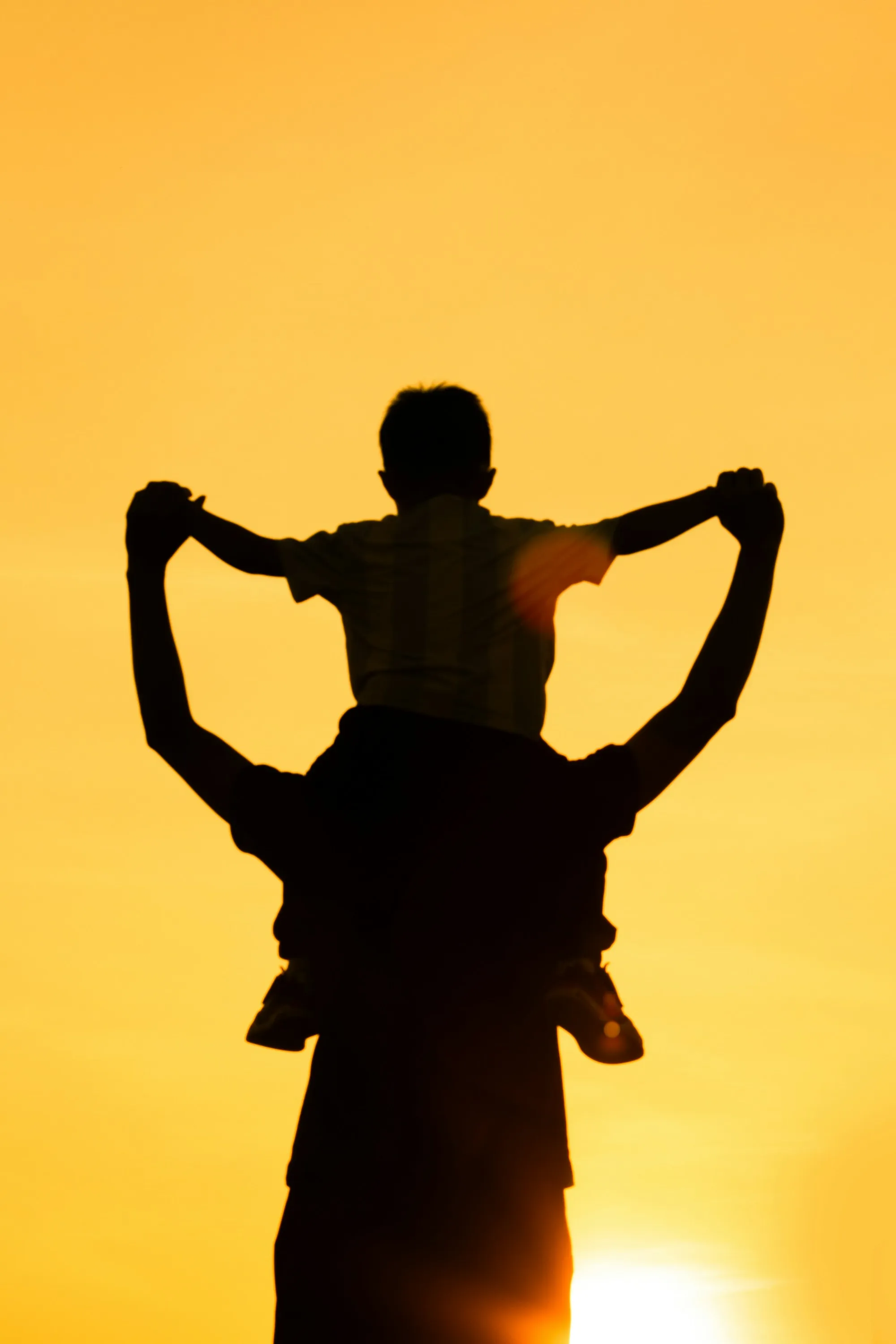 Silhouette of a child on a parent's shoulders
