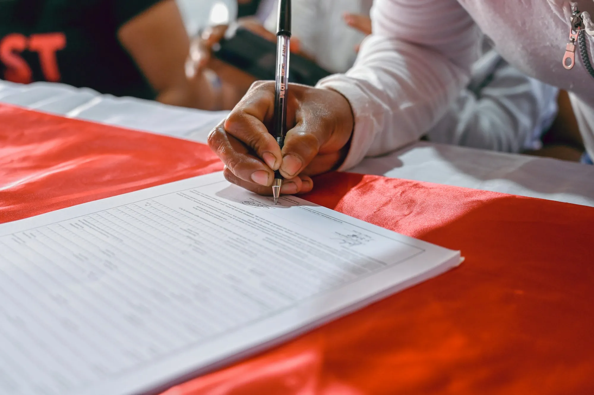 Hand signing a form on a red table